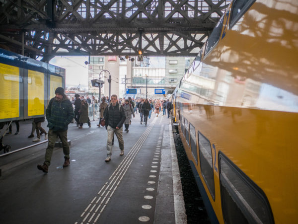 Treinreizigers lopen over perron op station Amsterdam Centraal.